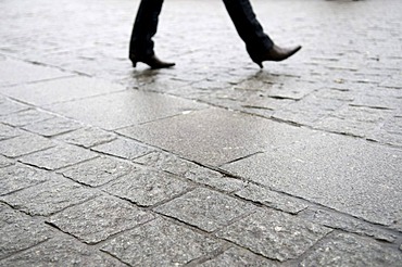 Feet with pointed shoes walking on wet pavement