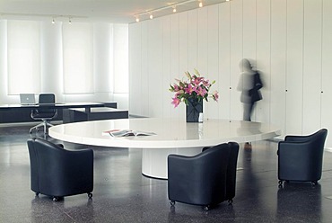 Round white conference table with empty, blue leather chairs and passing secretary