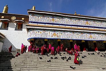 Tibetan monks in cowls of the Gelukpa order sitting on the stairs of the Assembly Hall, Tibetan Dukhang, Labrang Monastery, Xiahe, Gansu, China, Asia