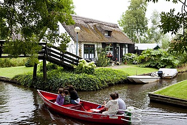 Traditional Dutch housing with garden beside the canal, tourists on a red boat visiting the village, Giethoorn, Flevoland, Netherlands, Europe