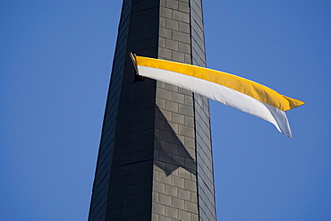 White and yellow flag fluttering from a church tower window against a steel blue sky