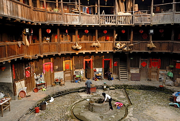 Chinese woman drawing water from the well in the courtyard of a wooden round house, Chinese: Tulou, adobe round house of the Hakka minority, Tianluokeng Building Group, Hukeng, Fujian, China, Asia