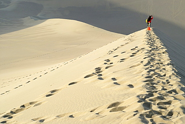 Young Chinese woman standing on the sand dunes of the Gobi Desert while photographing the Crescent Lake with the Chinese Pagoda in Dunhuang, Silk Road, Gansu, China, Asia