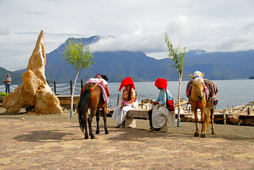 Ethnology, women of the Mosu ethnicity dressed in traditional costumes with horses on the shore, Luoshui, Lugu Hu Lake, Yunnan Province, People's Republic of China, Asia