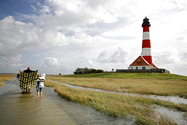 Tourists making a sail from a blanket in hurricane winds over the North Sea, path to Westerheversand Lighthouse, Schleswig-Holstein, Germany, Europe