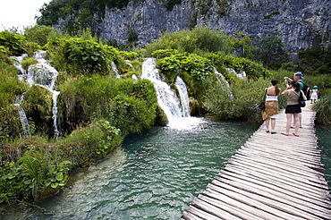 Tourists in front of a small waterfall in the cascade landscape of the Plitvice Lakes, Plitvice Lakes National Park, Croatia, Europe