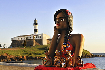 Traditional arts and crafts, clay figurine of a girl in love, namoradinha, and Forte de Santo Antonio da Barra fortress with Farol da Barra lighthouse, Salvador, Bahia, UNESCO World Heritage Site, Brazil, South America