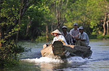 Woman wearing a traditional Vietnamese straw hat navigating a boat on the Mekong River, three men are seated behind her, Vinh Long, Mekong Delta, Vietnam, Asia