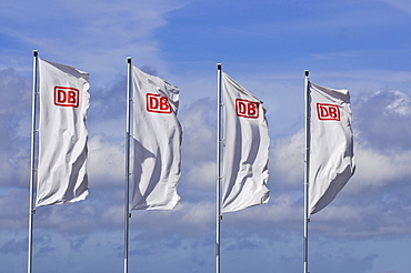 Four windblown white flags with the logo of DB, German Railways, in front of a sunny sky