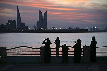 Skyline of the Corniche as seen from King Faisal Highway, Muharraq side, World Trade Center buildings, left, beside the towers of the Financial Harbour Complex, pedestrians walking along the Corniche in the evening, capital city, Manama, Kingdom of Bahrai