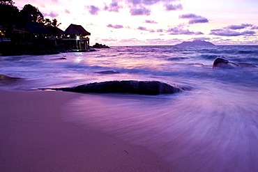 Typical granite rock of the Seychelles on the beach at dusk near Glacis, Sunset Beach Resort at back, island of Mahe, Seychelles, Indian Ocean, Africa