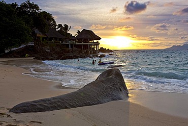 Typical granite rock of the Seychelles on the beach at dusk near Glacis, Sunset Beach Resort at back, island of Mahe, Seychelles, Indian Ocean, Africa