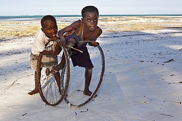 Children playing with old bicycle wheels on the beach of Pingwe, Zanzibar, Tanzania, Africa