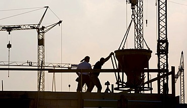 Construction workers working on a building site in front of a backdrop of several cranes in Waltrop, North Rhine-Westphalia, Germany, Europe