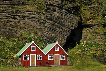 Red holiday homes in front of a rock wall, Vik, South Coast, Iceland, Europe