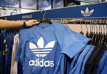 An employee holding a t-shirt with an Adidas logo in an outlet store of the Adidas Salomon AG in Herzogenaurach, Bavaria, Germany, Europe