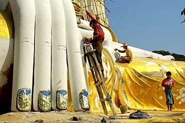 Renovation in progress painter paints the hand of big sitting Buddha Kyaikpun Bago Burma