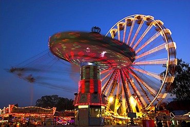 Amusement park during blue hour with Merry-Go-Round and big wheel in movement