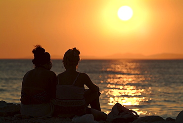 Two women on a beach watching the sunset over the ocean