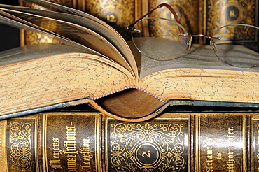 Reading glasses resting on an open page of an old encyclopaedia, leather bound books