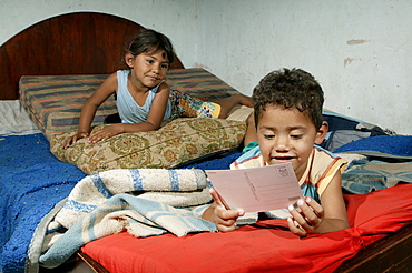 Guarani children sitting on the bed playing and reading in the poor area of Chacarita, Asuncion, Paraguay, South America