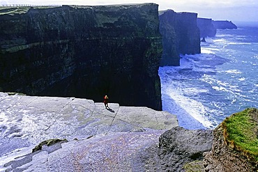 Tourist taking a photo while standing on the Cliffs of Moher, looking south, County Clare, Ireland, Europe