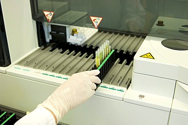 Hand in a sterile glove placing trays in a large piece of clinical equipment in a laboratory