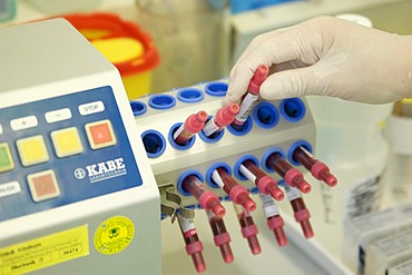 Hand in a sterile glove placing a tube of blood in a mixer in a laboratory