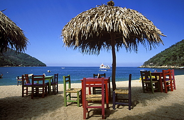 Bay and beach with wooden tables and chairs beneath thatched umbrellas, Bahia de Banderas, Playa Yelapa near Puerto Vallarta, Jalisco, Mexico