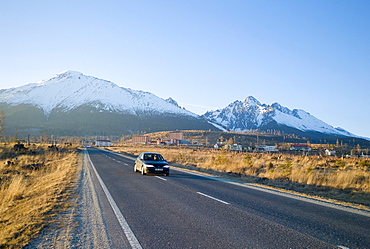 Car driving along a straight road leading to Tatranska Lomnica, with Carpathian Mountains, High Tatra peaks (back), near Vysoke Tatry, Slovakia