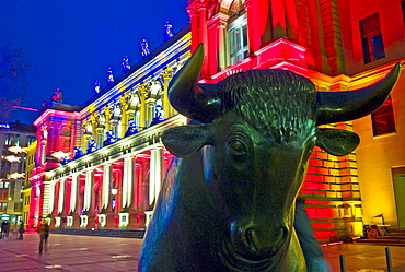 The bull of the Bull and Bear in front of the brightly lit Frankfurt Stock Exchange at night, illuminated by multicoloured spotlights for the Luminale, biannual lighting festival in Frankfurt, Germany