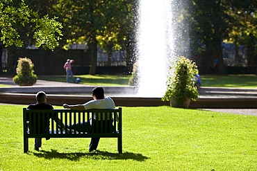 People in a park sitting on a bench in front of a fountain, Hesse, Germany