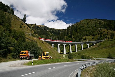 Construction work for Porta Alpina, the underground train stop in the Gotthard base tunnel, with driving work truck and a red train of the Matterhorn-Gotthard-Bahn (background), Sedrun, Grisons, Switzerland