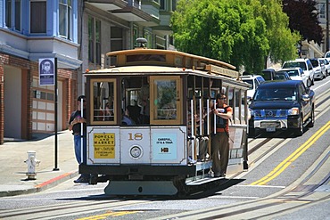 Cable Car with tourists in the open doors on the steep streets in the hills of San Francisco, California, USA