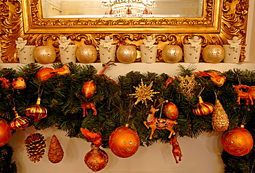 Mantelpiece showing edge of gold-framed mirror, Christmas ornaments hanging from pine sprigs from mantel