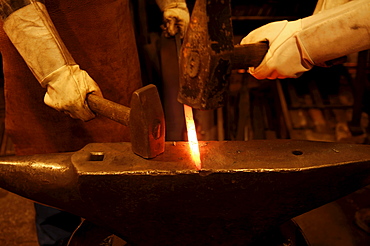 Glowing iron rod being hammered into shape against an anvil by two smiths wearing long white leather gloves, Industrial Museum, Lauf an der Pegnitz, Bavaria, Germany, Europe