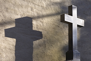 Cross throwing a shadow at a grave, Alter Suedfriedhof, old cemetery in Munich, Bavaria, Germany