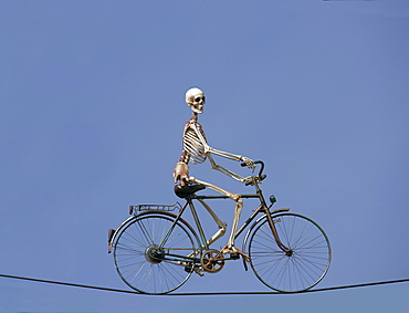 Skeleton riding a bike on a wire cable