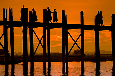 Buddhist monks walking over an old teak bridge at sunset, Mandalay, Myanmar (Burma), Southeast Asia