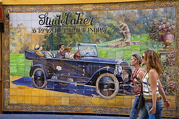 Girls passing a wall of tiles depicting a Studebaker car in Calle Tetuan street, Seville, Andalusia, Spain, Europe