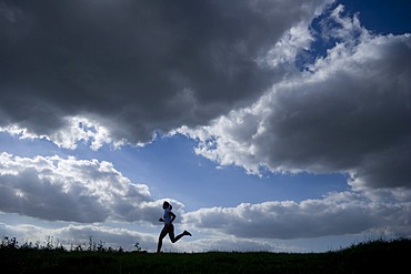 Running woman as a silhouette in front of a sky with dark clouds