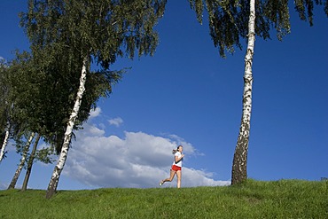 Running woman on a dam in front of blue sky