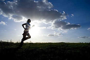 Running woman as a silhouette in front of a sky in back light