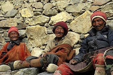 Three friendly man in traditional dress made of wool sit at a wall Phu Nar-Phu Annapurna Region Nepal