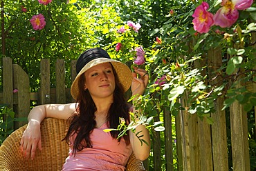 Young women is sitting on a chair in the garden and enjoys the sun