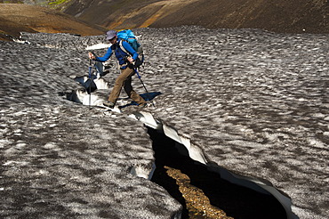 Female hiker walking on a snow slab, on the Laugavegur hiking trail, Hrafntinnusker-âˆšÃ…lftavatn, Fjallabak Nature Reserve, Highlands of Iceland, Iceland, Europe