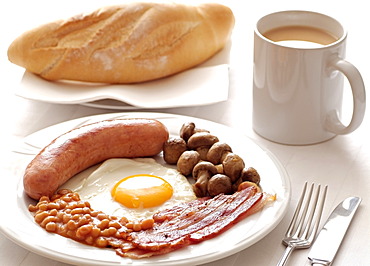 Traditional English Cooked Breakfast of Sausage, Egg, Bacon, Mushrooms and Beans. Served with a Mug of Tea.