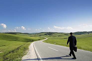 Businessman walking along a lonely country road, rear view