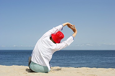 Woman wearing a red hat relaxing and stretching on the beach, Sylt island, Schleswig-Holstein, Germany, Europe