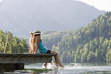 Young women sitting on a landing stage on Lake Schwansee near Fuessen, Allgaeu region, Bavaria, Germany, Europe